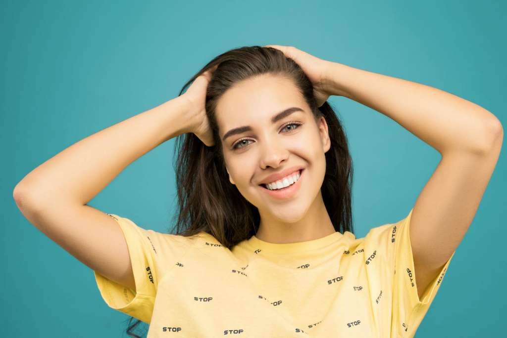 A cheerful woman in a yellow shirt poses against a teal background.
